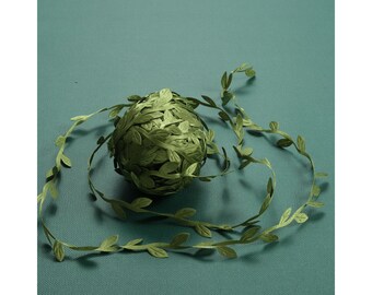 Puede incluir: Guirnalda de hojas verdes de tela, con una bola de guirnalda en el centro. La guirnalda está sobre un fondo verde.