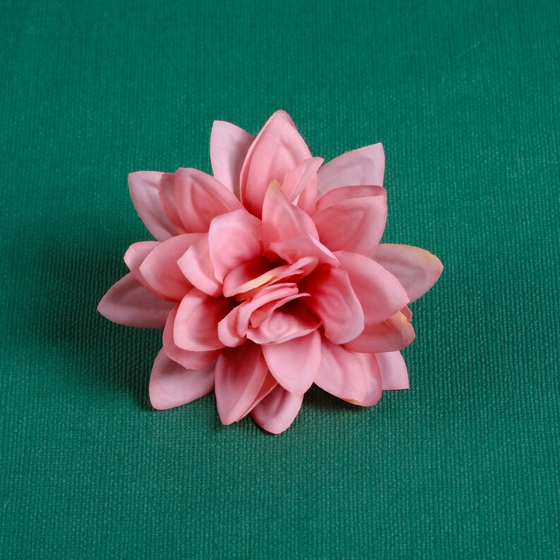 Puede incluir: Una flor artificial rosa con m&uacute;ltiples p&eacute;talos, que se asemeja a una dalia, sobre un fondo verde.