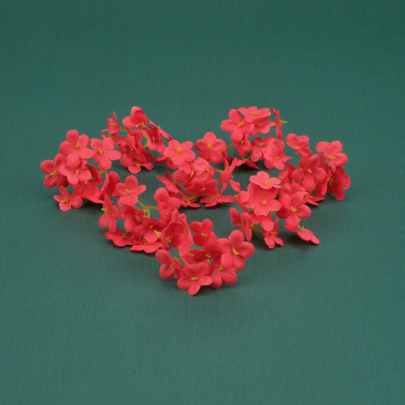 May include: A cluster of small, bright pink artificial flowers arranged in a heart shape on a green background.