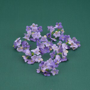 May include: A cluster of purple and white artificial flowers arranged in a star shape on a green background.