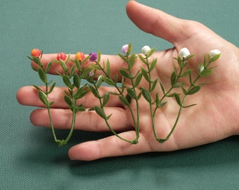 May include: A hand holding five sprigs of artificial greenery with small flowers. The flowers are white, orange, and purple.