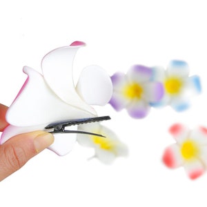 May include: A white flower hair clip with a pink and white flower design. The clip is made of plastic and has a black metal clip.