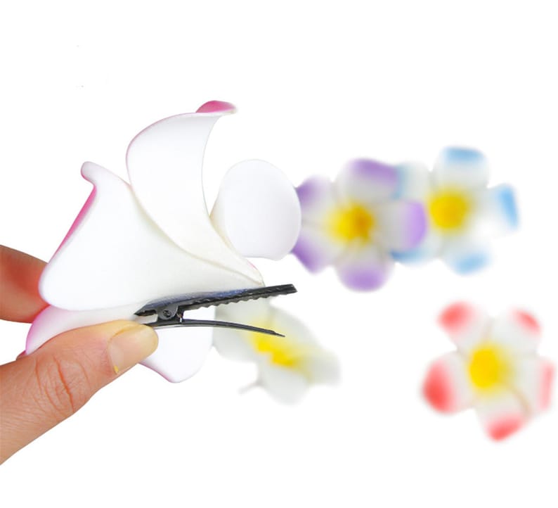 May include: A white flower hair clip with a pink and white flower design. The clip is made of plastic and has a black metal clip.