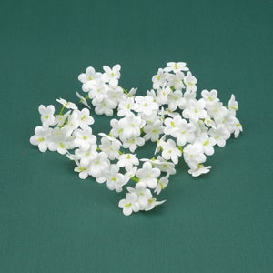 May include: A cluster of white artificial flowers with green stems, arranged in a heart shape on a green background.