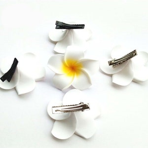 May include: Four white flower hair clips with yellow centers. Two clips have black clasps and two have silver clasps.