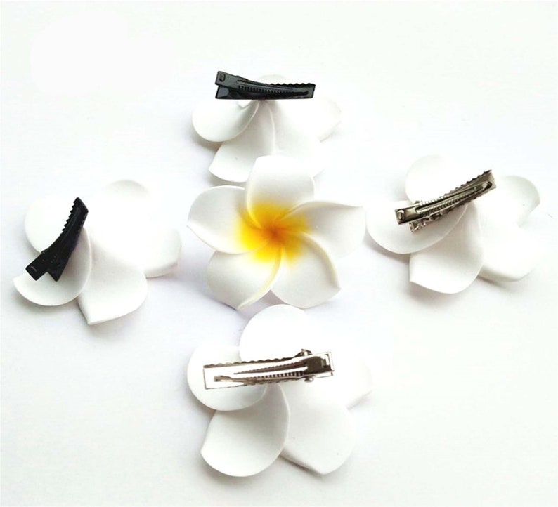 May include: Four white flower hair clips with yellow centers. Two clips have black clasps and two have silver clasps.