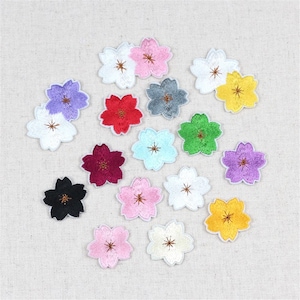 Może przedstawiać: Zestaw 15 haftowanych naszywek w kształcie kwiatów w różnych kolorach, w tym różowym, czerwonym, zielonym, niebieskim, żółtym, czarnym, białym i fioletowym. Naszywki mają kształt pięciopłatkowych kwiatów z kółkiem w środku.