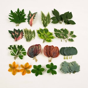 May include: Assortment of 18 artificial leaves in various colors and textures, including green, red, brown, and yellow. The leaves are arranged in rows on a white background.