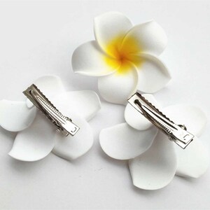 May include: Three white flower hair clips with yellow centers. The clips are made of fabric and have a metal clip on the back.