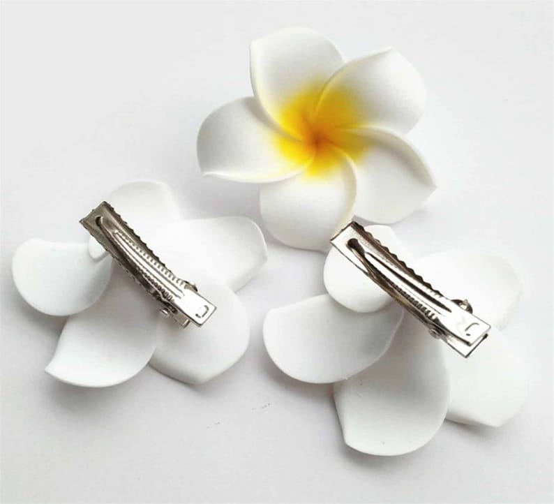 May include: Three white flower hair clips with yellow centers. The clips are made of fabric and have a metal clip on the back.