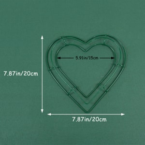 K&ouml;nnte beinhalten: Eine gr&uuml;ne, herzf&ouml;rmige Kranzform aus Metall mit den Ma&szlig;en 20 cm x 15 cm. Die Kranzform besteht aus Draht und hat eine doppelte Schicht.