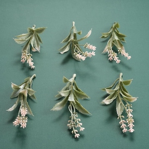 May include: Six sprigs of artificial lavender with green leaves and pink flowers. The sprigs are arranged in two rows of three on a green background.