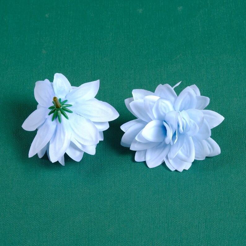 Puede incluir: Dos flores artificiales de color azul claro con un centro verde. Las flores est&aacute;n sobre un fondo verde.