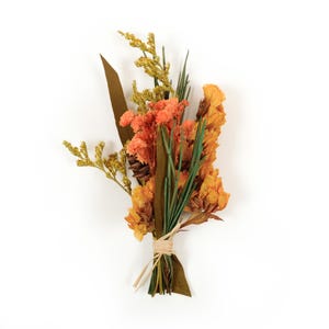 Peut inclure: Un petit bouquet de fleurs séchées aux tons orange, jaune et marron, noué avec de la ficelle. L'arrangement comprend diverses textures, telles que des fleurs séchées, des feuilles et des brins, créant une esthétique rustique et naturelle. Un petit cône de pin est également inclus.