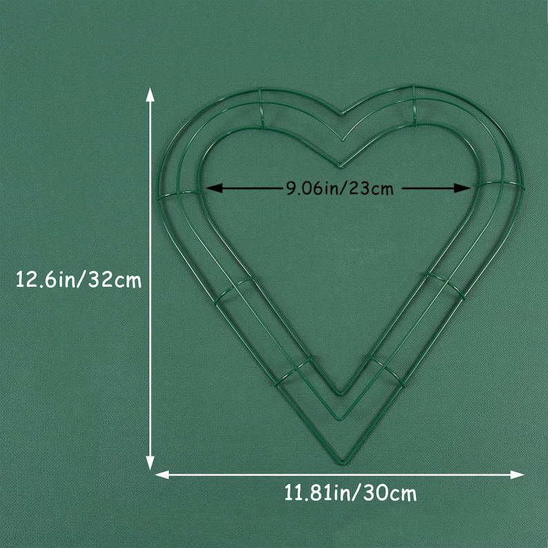 K&ouml;nnte beinhalten: Ein gr&uuml;ner, herzf&ouml;rmiger Kranzrahmen aus Metall mit einer H&ouml;he von 32 cm, einer Breite von 23 cm und einer Breite von 30 cm an der Unterseite.