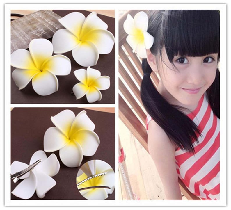 May include: Four white and yellow plumeria flower hair clips. The flowers are made of fabric and have a realistic appearance. The clips are attached to the back of the flowers.