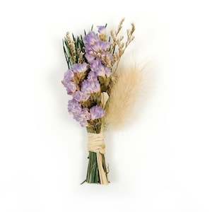 Peut inclure: Un petit bouquet de fleurs séchées comprenant de la statice lavande, de l'herbe de la pampa beige et d'autres verdures séchées. Les tiges sont liées avec de la ficelle naturelle, créant un arrangement floral rustique.