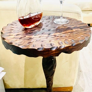 May include: A dark brown wooden side table with a carved, scalloped top and a twisted, ornate base. A clear glass decanter filled with dark liquid and a stemmed glass filled with dark liquid are on the table.