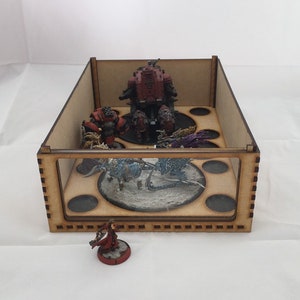 May include: A wooden box with a glass front, containing miniature figures and bases. The box has a brown wood finish and a black interior. The figures are painted in various colors, including red, blue, and purple.
