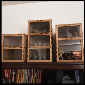 May include: Four wooden display cases with glass fronts, stacked on a shelf. The cases are filled with miniature figurines. The cases have a decorative border around the edges.