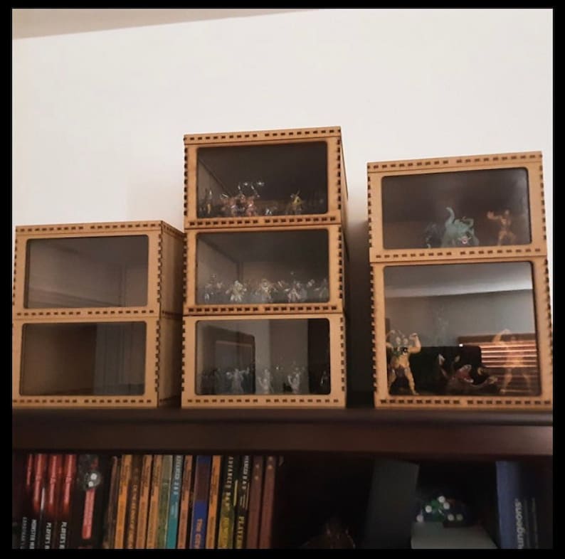 May include: Four wooden display cases with glass fronts, stacked on a shelf. The cases are filled with miniature figurines. The cases have a decorative border around the edges.