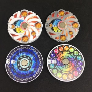 May include: Four round, colorful, printed game pieces with a magnet in the center. Each piece has a number "0" printed on it. The pieces have different designs, including a swirling pattern with orange and white, a swirling pattern with gray and white, a blue and white pattern with chains, and a rainbow pattern with circles.