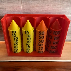 Könnte beinhalten: Ein roter Plastikbehälter mit drei Stapeln bunter Zählchips. Die Stapel sind mit den Zahlen 10, 50 und 100 beschriftet.