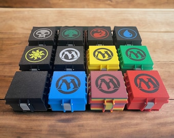 May include: Twelve small, square boxes with different colored lids and black and white symbols on the top. The symbols include a skull, a tree, a flame, a drop of water, a sun, and the letter "M".