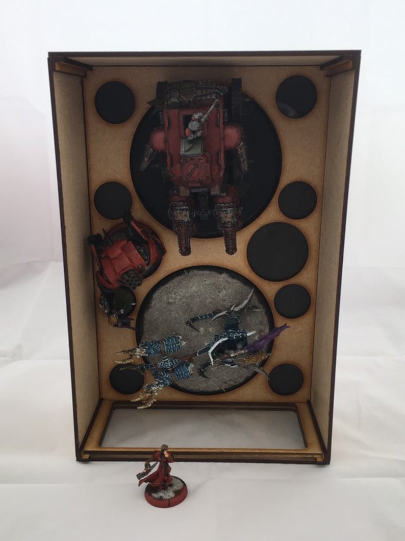 May include: A wooden box with a clear plastic window, containing miniature figures and vehicles. The box has a brown wood finish and is filled with circular cutouts. The figures are painted in various colors, including red, blue, and green.