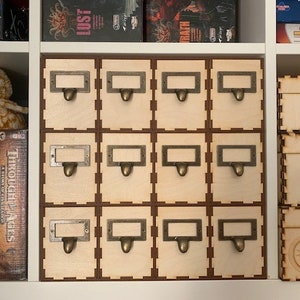 May include: A set of 12 wooden storage boxes with labels and metal handles. The boxes are arranged in a 3x4 grid and are all the same size. The boxes are a light wood color and have a natural finish.