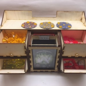 May include: Wooden organizer with multiple drawers and compartments for storing game pieces and cards. The top has three circular tokens with a swirling design. The drawers are labeled "presents", "bonus", and "player actions".