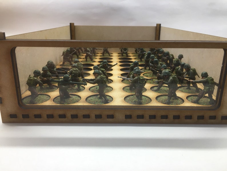May include: A wooden display case with a clear front panel, showcasing a collection of miniature figures in military uniforms. The figures are arranged on circular bases and are positioned in a battle formation.