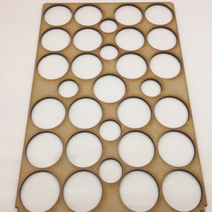 May include: A wooden board with a grid of circular cutouts of varying sizes. The board is light brown and has a natural wood finish.