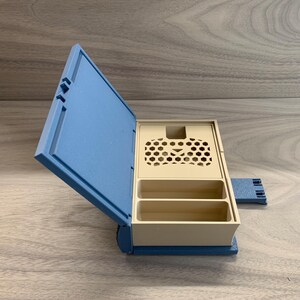 以下が含まれることがあります： 蓋にハニカム模様が施された青とベージュの収納ボックス。ボックスには2つのコンパートメントとヒンジ付きの蓋があります。