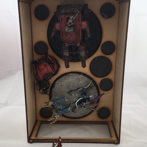 May include: A wooden box with a clear plastic window, containing miniature figures and vehicles. The box has a brown wood finish and is filled with circular cutouts. The figures are painted in various colors, including red, blue, and green.