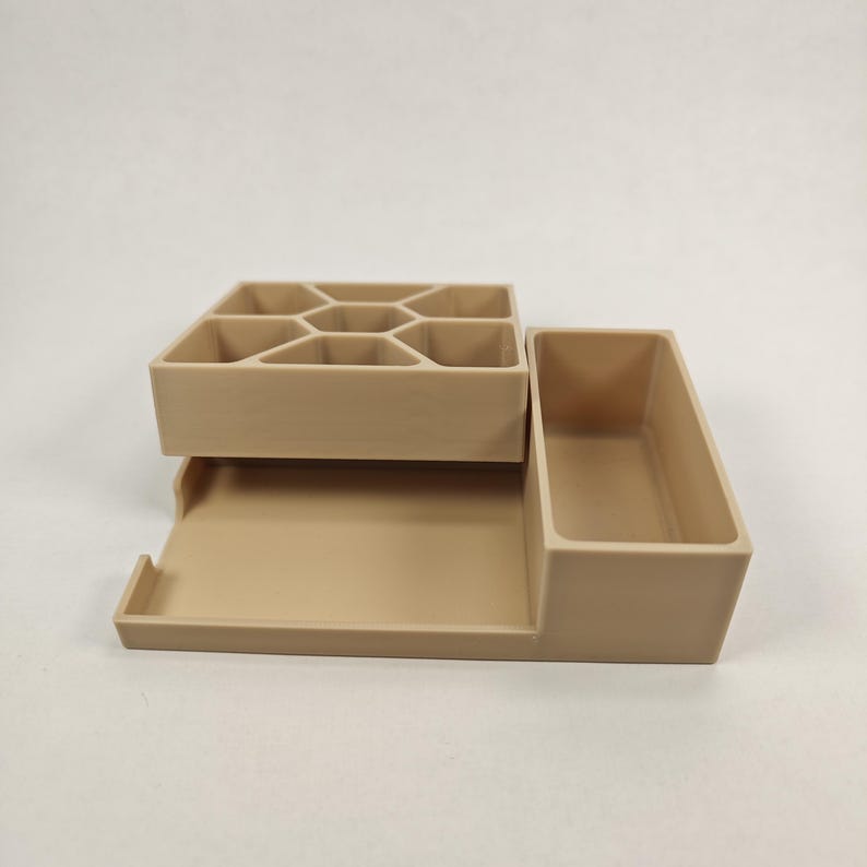 以下が含まれることがあります： ベージュのプラスチック製のデスクオーガナイザーで、複数のコンパートメントがあります。オーガナイザーは、9つの小さなコンパートメントを持つ上部セクションと、より大きなコンパートメントと長く狭いコンパートメントを持つ下部セクションがあります。
