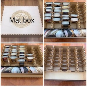 May include: A wooden box with a lid that has a circular design and the text "Mat box" engraved on it. The box is divided into compartments for storing cards. The box is shown open with a roll of fabric inside.