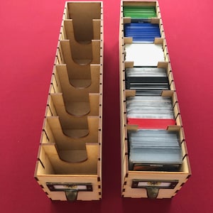 May include: Two wooden card storage boxes with dividers. The boxes are made of light brown wood and have a metal handle. The boxes are filled with cards of different colors.
