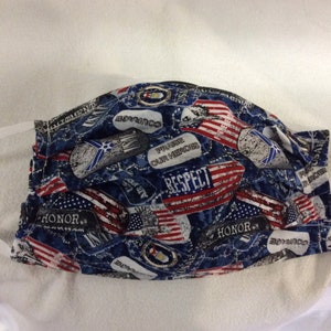 Puede incluir: Una mascarilla facial azul y roja con un tema patriótico. La mascarilla presenta banderas americanas, estrellas y palabras como "Honor", "Respeto" y "Valor".