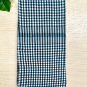 Puede incluir: Una tela a cuadros blancos y negros con una franja azul en el medio. La tela est&aacute; doblada por la mitad y colocada sobre una superficie de madera.