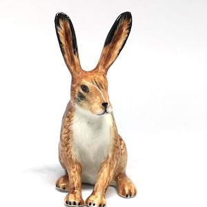 May include: A small ceramic figurine of a brown and white rabbit sitting with its ears upright. The rabbit has black markings on its ears and a white chest.