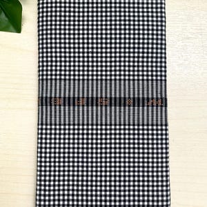 Puede incluir: Tela a cuadros negros y blancos con un fino borde tejido naranja y negro.