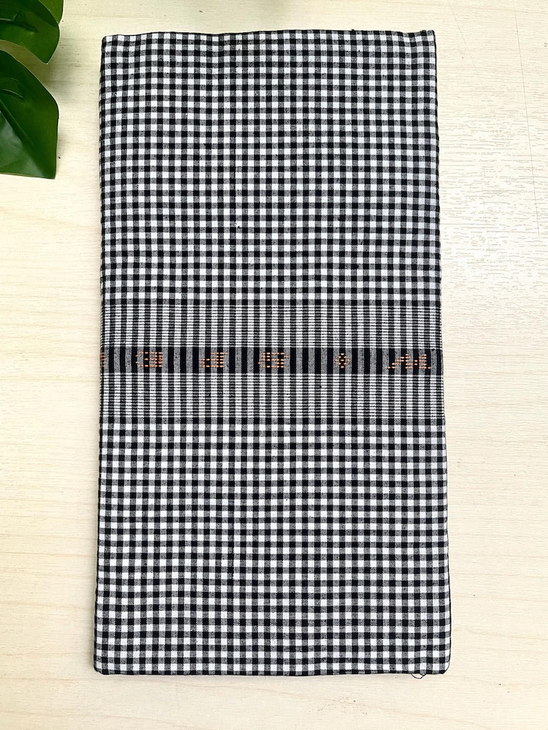 Puede incluir: Tela a cuadros negros y blancos con un fino borde tejido naranja y negro.