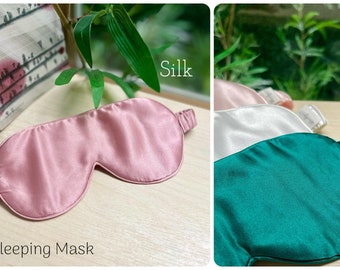 May include: Three silk sleeping masks in pink, white, and green. The masks are made of soft, smooth silk and have elastic straps. The text "Silk" is written above the masks and the text "Sleeping Mask" is written below the pink mask.