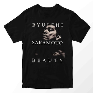 Könnte beinhalten: Schwarzes T-Shirt mit einem Graustufen-Porträt von Ryuichi Sakamoto und den Worten "RYUICHI SAKAMOTO BEAUTY" in Weiß. Das T-Shirt hat einen Rundhalsausschnitt.