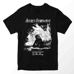 May include: Black t-shirt with a white graphic featuring a hooded figure in a forest scene. The text "Secret Stairways" is above the image, and "Enchantment Of The Ring" is below.