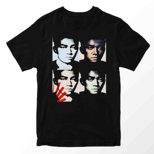 Könnte beinhalten: Schwarzes T-Shirt mit einem Pop-Art-Design, das vier Porträts einer Person zeigt. Die Porträts sind in einem Raster angeordnet, mit unterschiedlichen Farbschemata. Ein Porträt hat rote und weiße Linien. Das Shirt ist aus weichem Material.