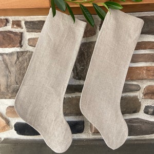 May include: Two beige linen Christmas stockings hanging on a brick fireplace mantel.