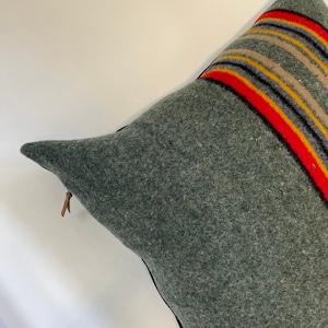 Puede incluir: Una almohada verde con cierre de cremallera y un patrón de rayas coloridas en un lado. La almohada está hecha de una tela suave y peluda.