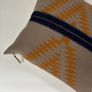Puede incluir: Una almohada de color marrón y dorado con una franja azul oscuro en el centro. La almohada tiene una cremallera.